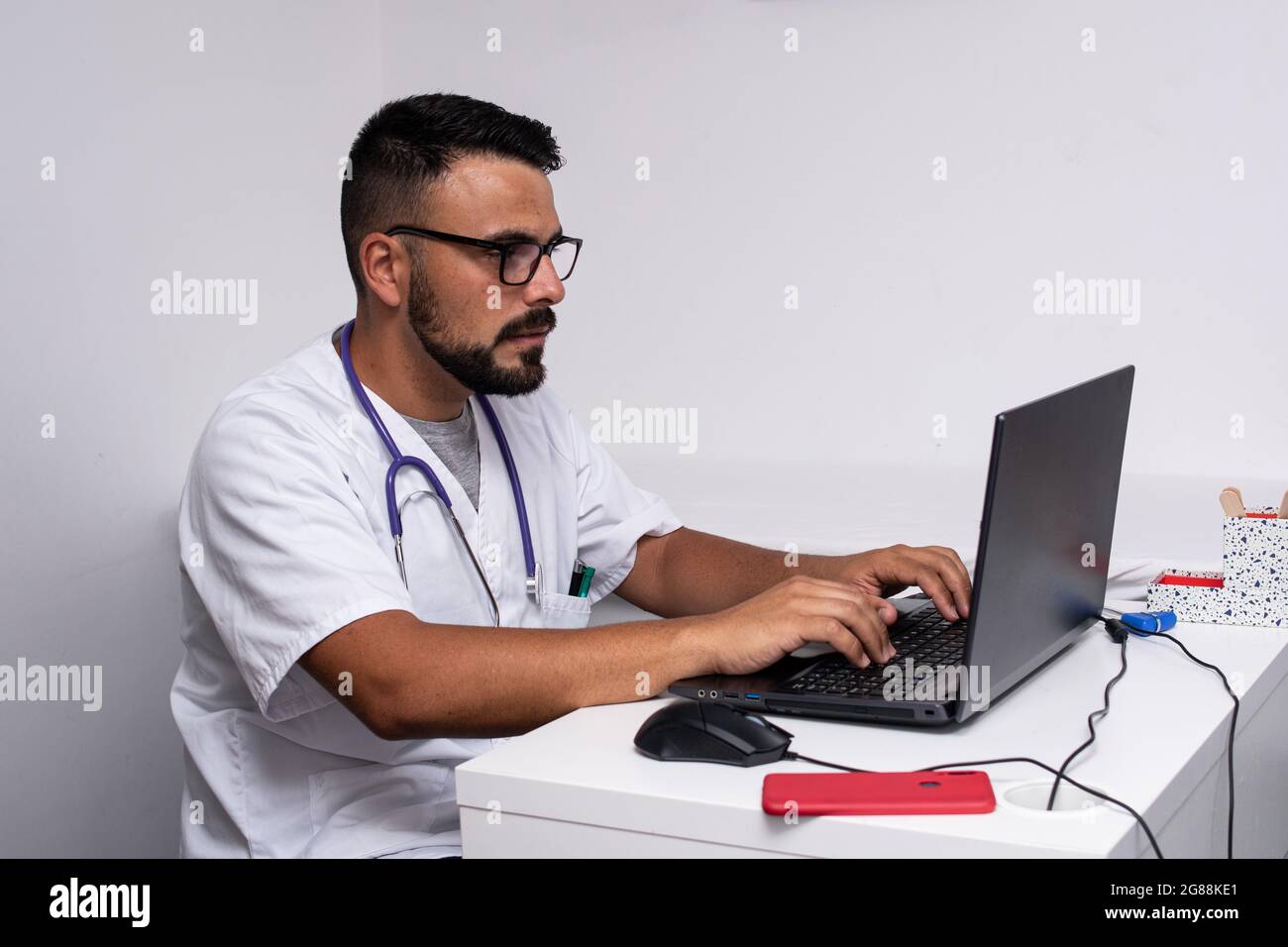 Junger kaukasischer Arzt mit Bart und Brille in seinem Büro Stockfoto