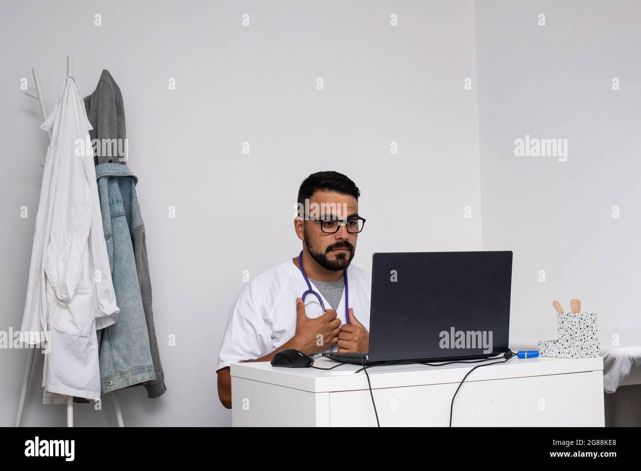 Junger kaukasischer Arzt mit Bart und Brille in seinem Büro Stockfoto