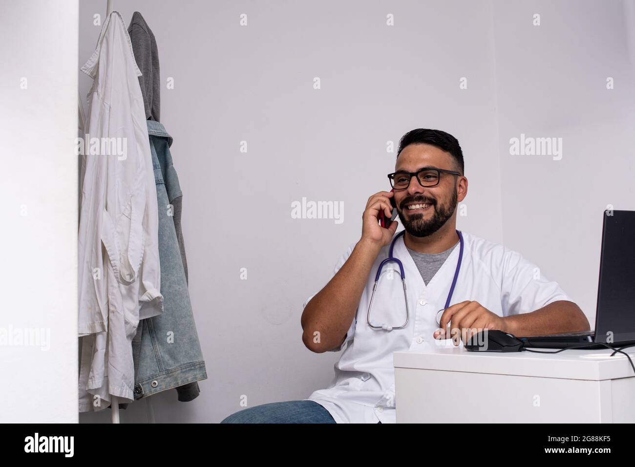 Kaukasischer Arzt, der in der Konsultation mit seinem Smartphone anruft Stockfoto