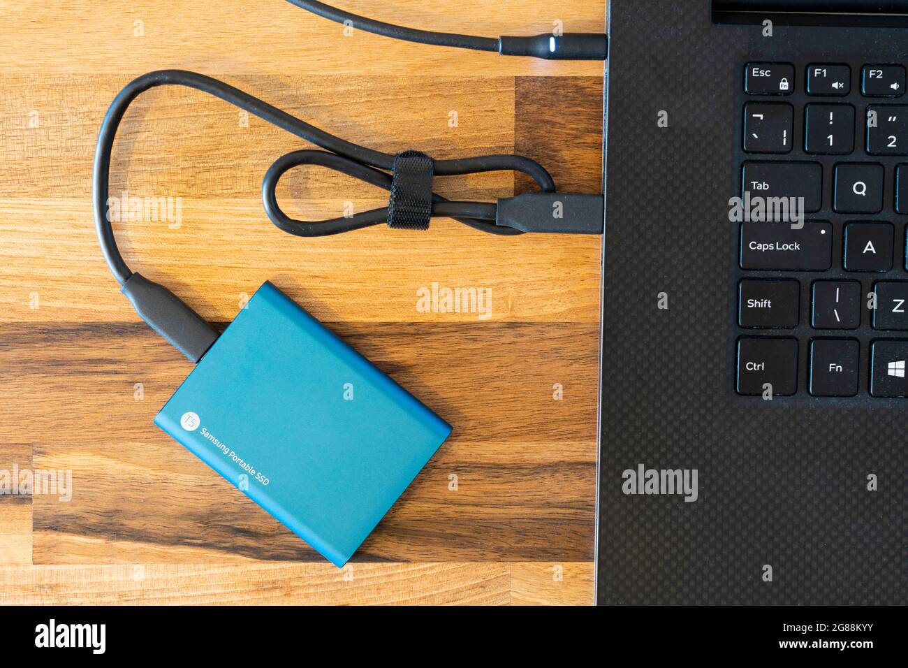 Ein blaues, mit 500 GB verschlüsseltes, externes SSD-Laufwerk (Solid State Drive) von Samsung für die Datensicherung mit einem USB-C-Verbindungskabel, das es mit einem Laptop verbindet Stockfoto