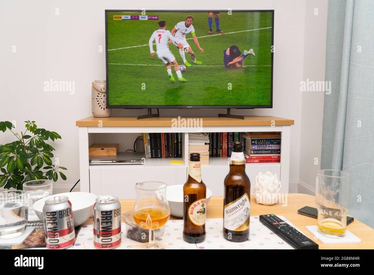 Ein breitbildfernseher, auf dem Harry Kane während des UEFA-Fußballfinales der Euro 2020 mit England gegen Italien am Ball mit Bier auf einem Tisch zu sehen ist. VEREINIGTES KÖNIGREICH Stockfoto