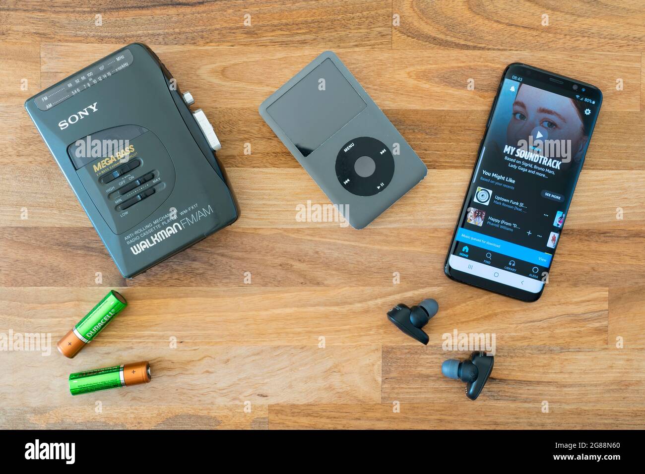 Weiterentwicklung der tragbaren Musik-Technologie: Ein veralteter Sony Walkman mit Batterien, ein veralteter Apple iPod und Amazon Music auf einem Android-Smartphone Stockfoto