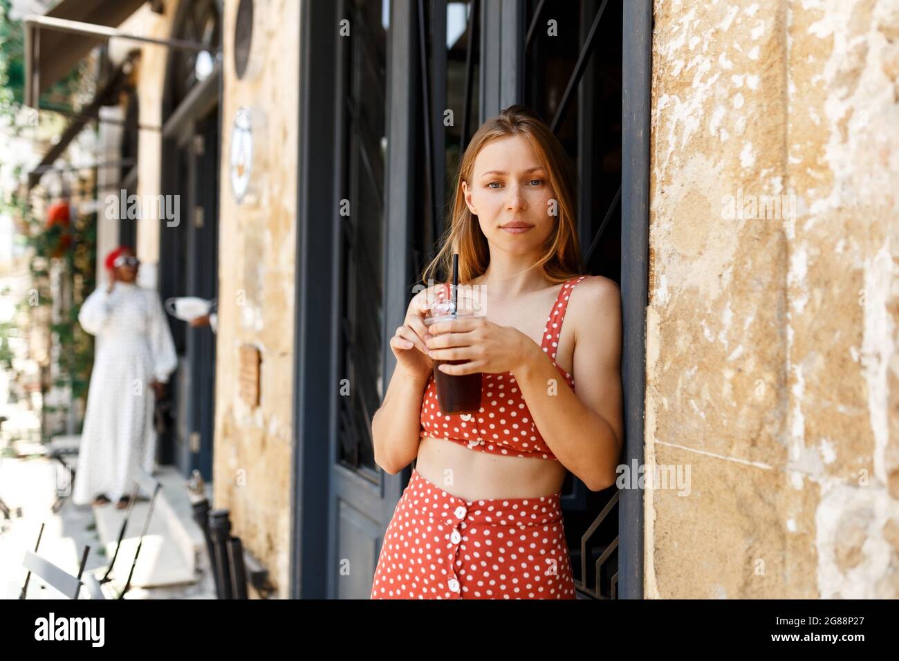 Ein hübsches, junges Hipster-Mädchen mit einer Tasse Getränk, das neben dem Sommercafé auf der Straße steht. Leider schaut in die Ferne.Nehmen Sie eine Kaffeebremse.psychische Gesundheit PR Stockfoto