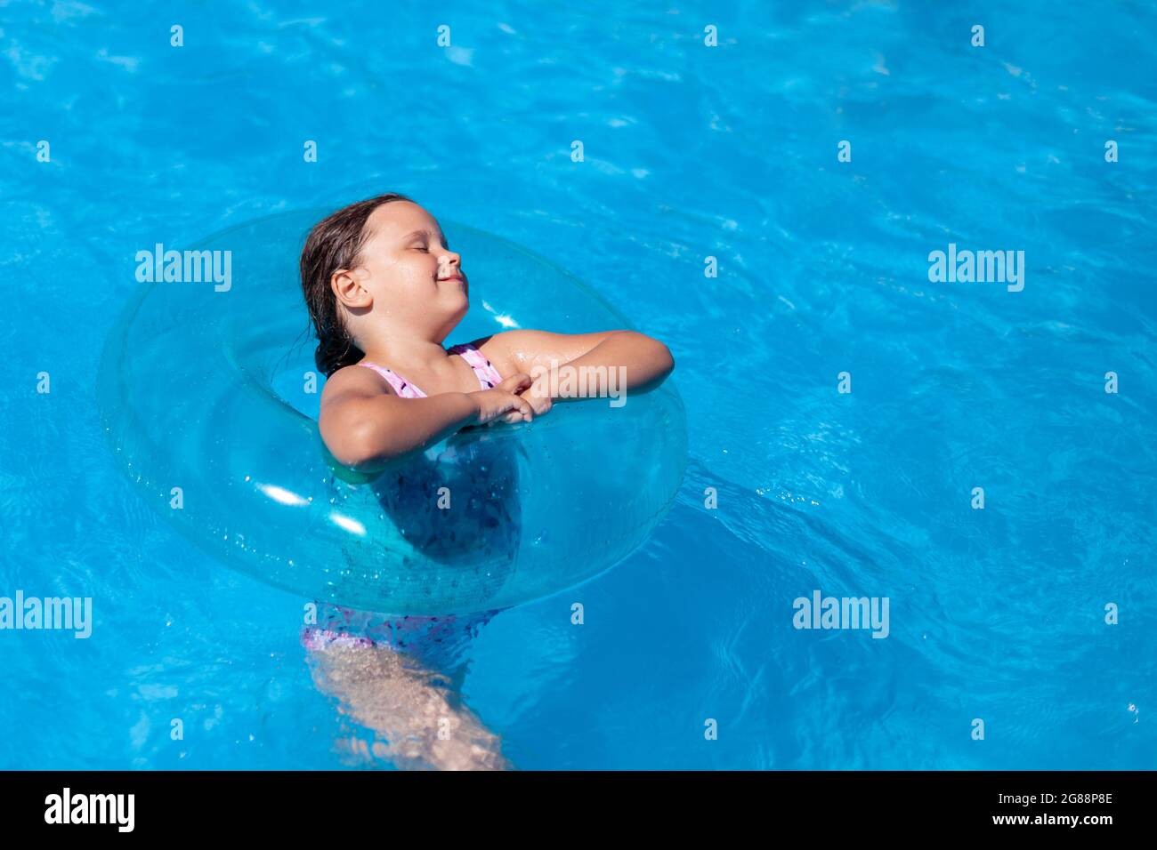 Minimalistischer Trend, blauer aufblasbarer Schwimmkreis auf dem blauen Wasser des Pools, ein glückliches Mädchen, das an einem heißen Sommertag die Kühle des Wassers genießt Stockfoto