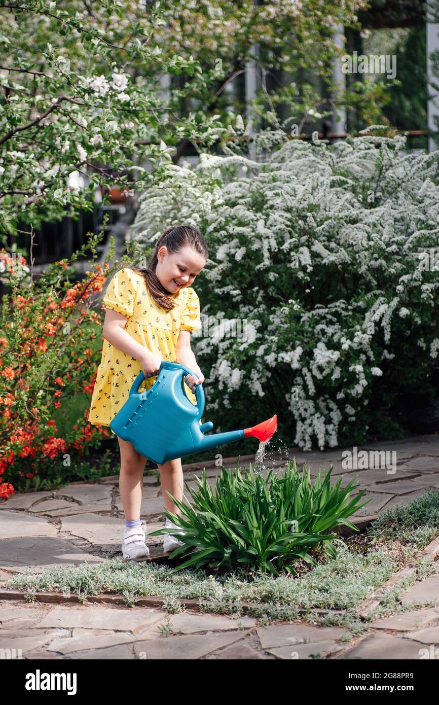 Ganzkörperportrait eines glücklichen Mädchens, das an einem warmen, hellen Tag Blumen in einem frühlingsblühenden Garten wässert Stockfoto