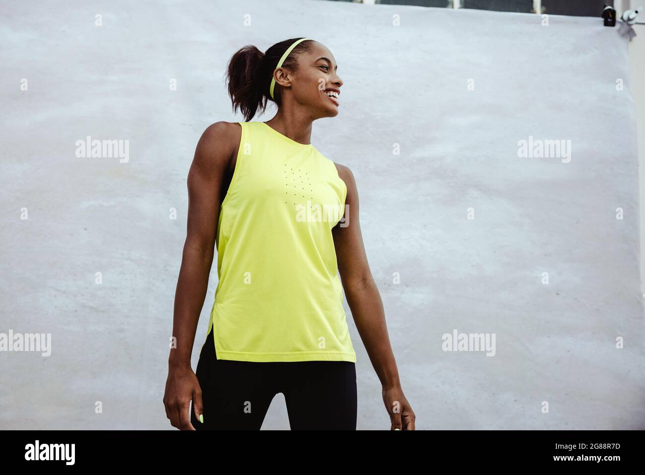 Afrikanische Frau in Sportkleidung, die wegschaut und lächelt. Athletin, die vor weißem Hintergrund steht. Stockfoto