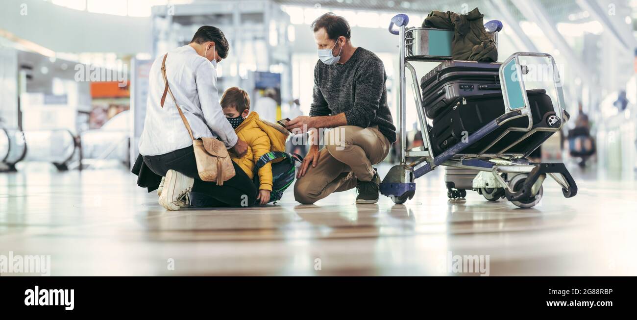 Weitwinkelansicht einer Frau, die ihren Sohn und Ehemann nach einer Pandemie am Flughafen trifft. Familie am Flughafen mit Gepäck an der Seite. Stockfoto