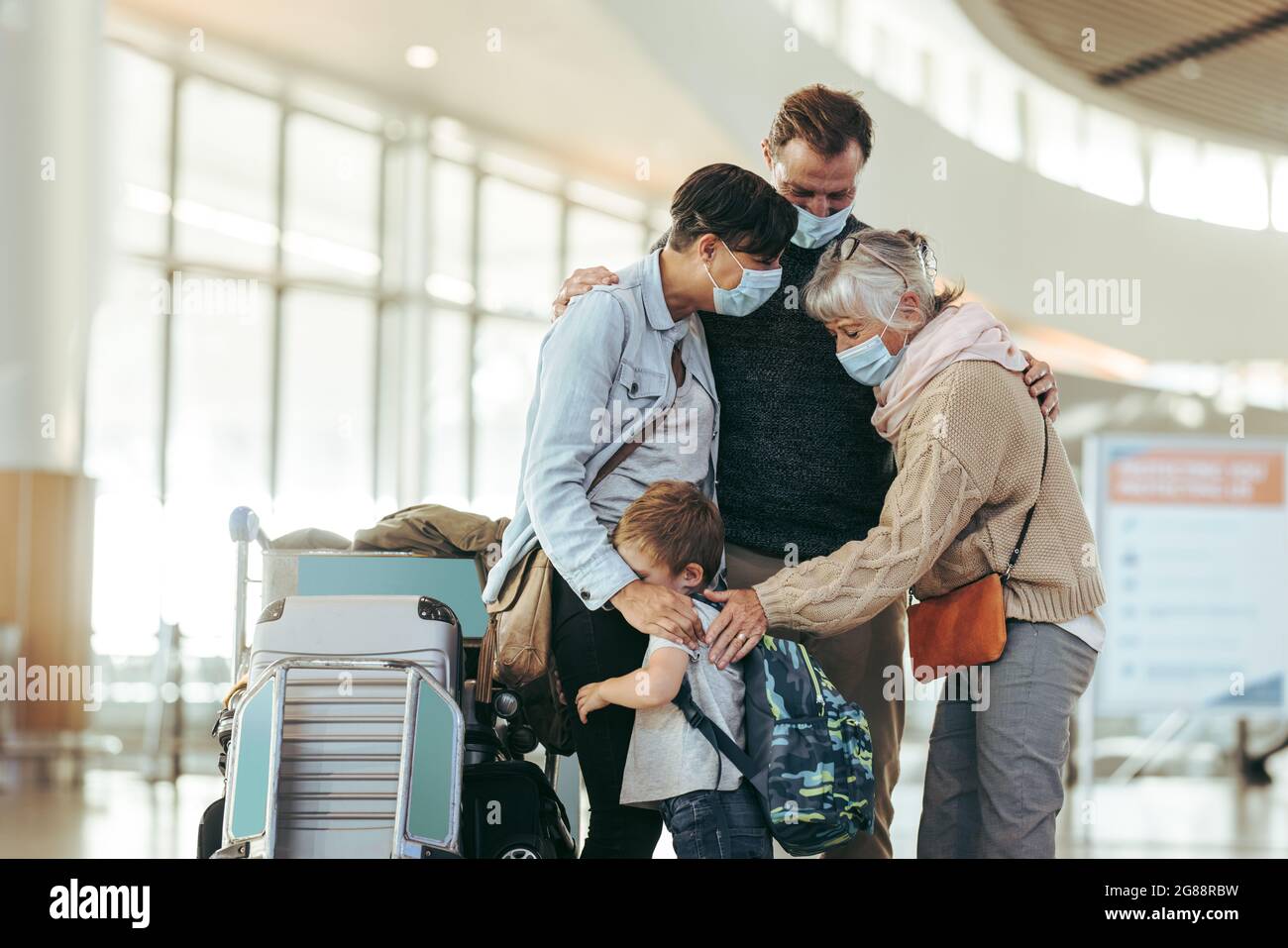 Ältere Frau begrüßt und begrüßt die Familie, die nach der Sperrung durch die Pandemie am Flughafen ankommt. Das Paar und sein Kind werden von der Mutter am Flughafen begrüßt. Al Stockfoto