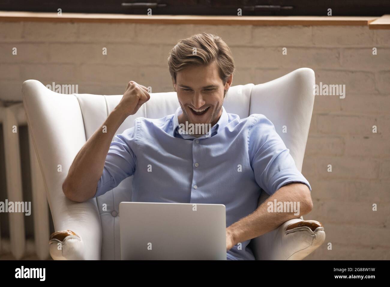 Junger Mann, der sich im Sessel entspannt, mit Laptop, der Lotteriegewinnerin wird Stockfoto