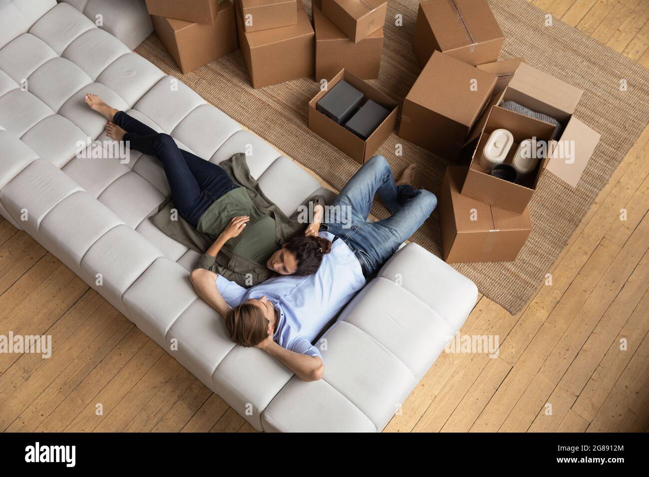 Junge Ehepartner Moderne Wohnungseigentümer kuscheln auf der Couch zwischen Boxen Stockfoto