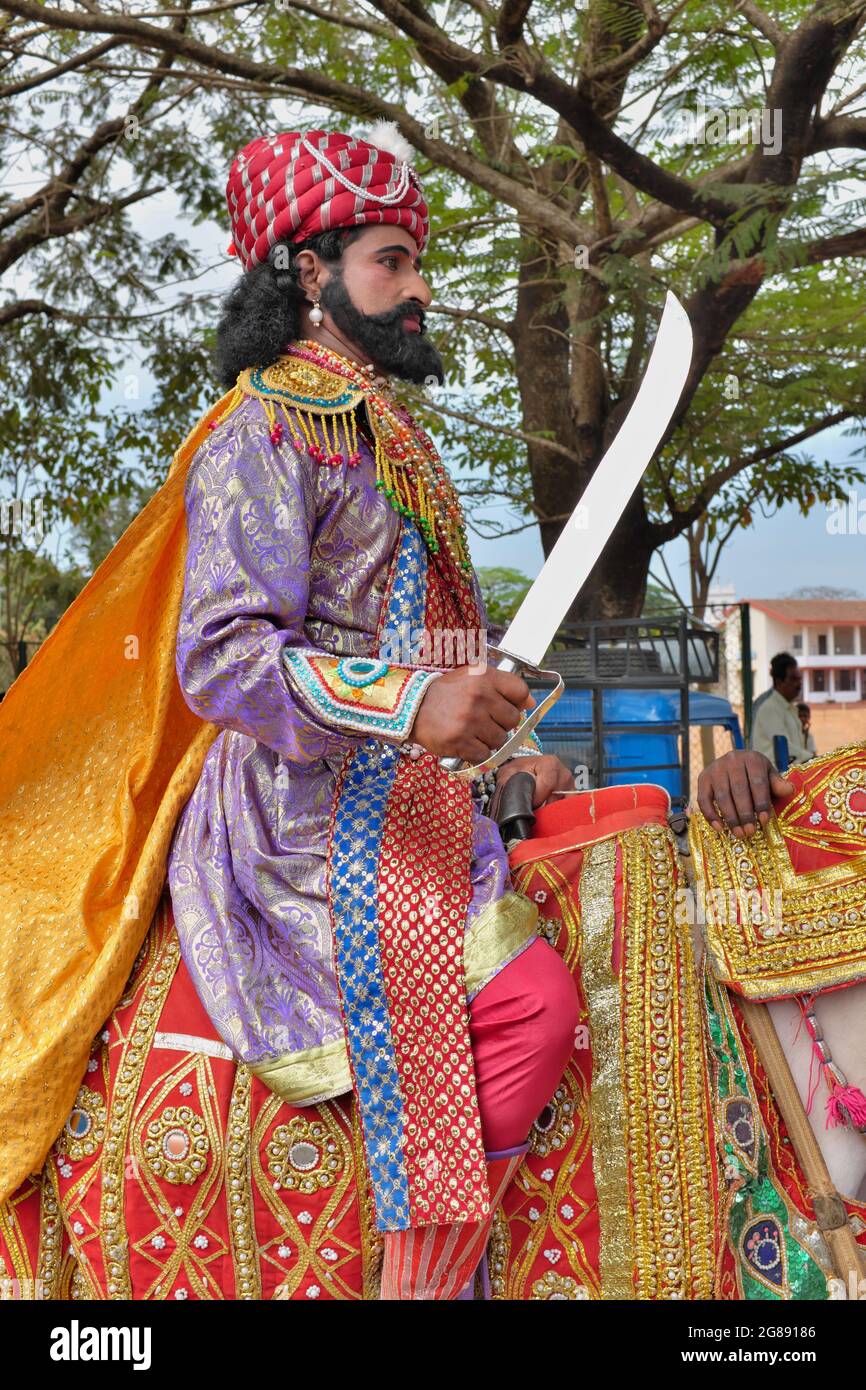 Ein Mann, der als historischer Kriegerkönig gekleidet ist, fährt in einer Prozession ein Pferd, das ein historisches Ereignis in Mangalore (Mangaluru), Karnataka, Indien, vorführt Stockfoto
