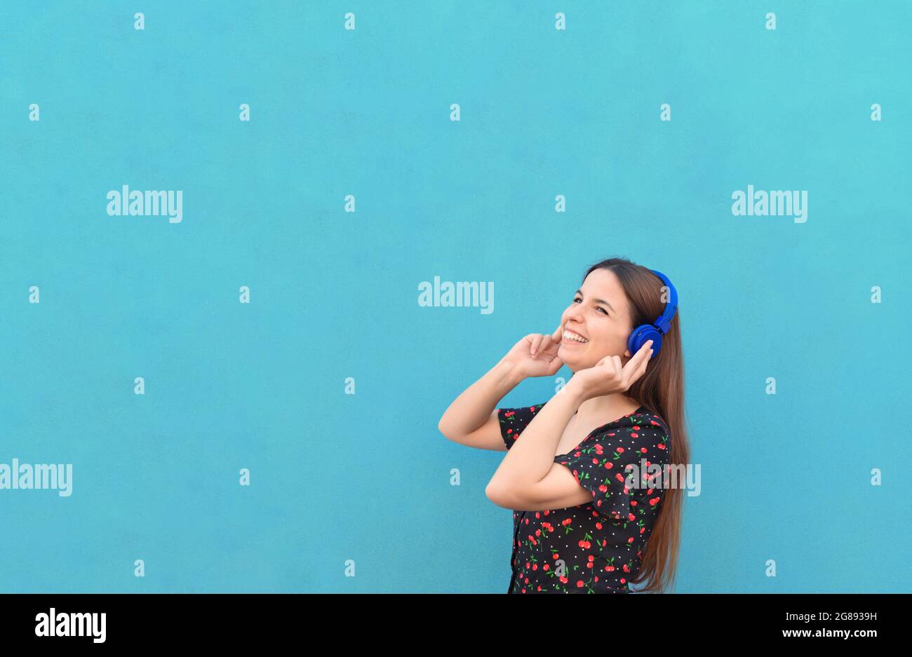 Nahaufnahme - Portrait junge schöne Frau in lässigem Outfit mit Kopfhörern vor blauem Hintergrund - Sommer, Freude, Entspannung, Konzept über g Stockfoto