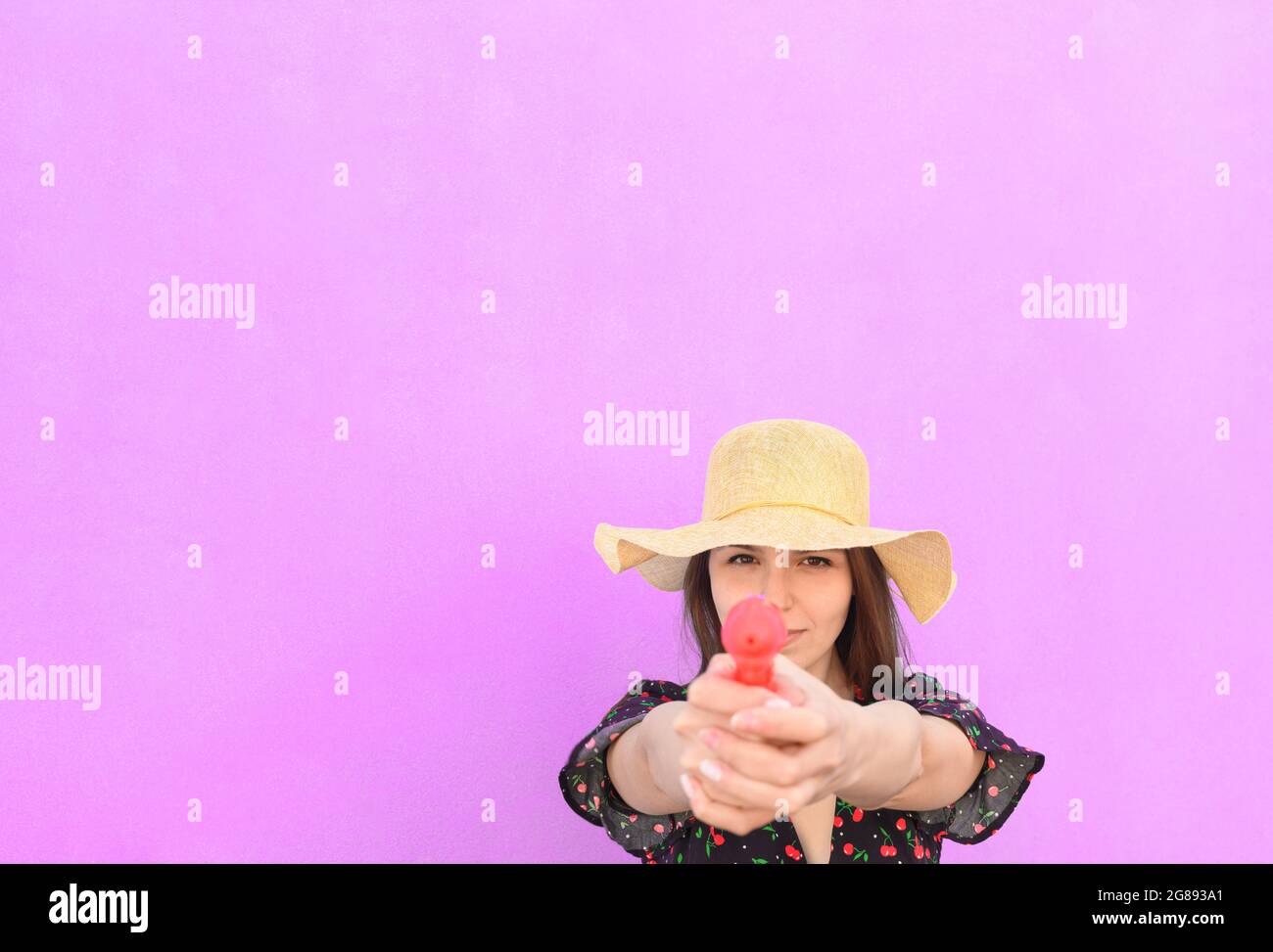 Portrait junge schöne Mädchen in Casual Outfit halten Spielzeug Wasserpistole und posiert isoliert auf dem rosa Hintergrund - Sommer, Freude, entspannen, Konzept - Raum Stockfoto