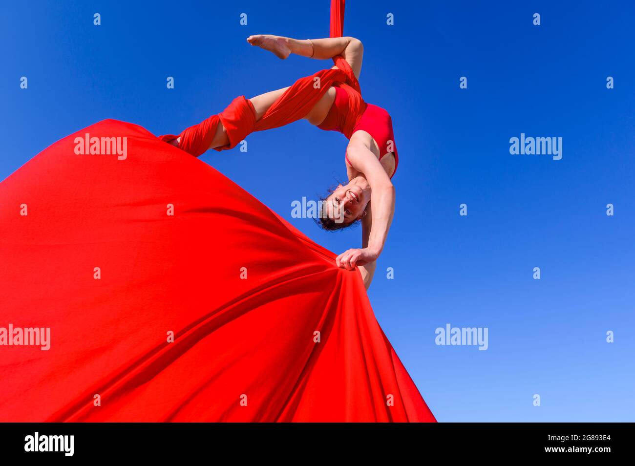 Outdoor-Aktivität der Turnerin, die Training auf roten Luftseiden und Bändern am Himmel durchführt - Mädchen, die Tanz in der Luft mit roten Stoffen, Sport, Stockfoto