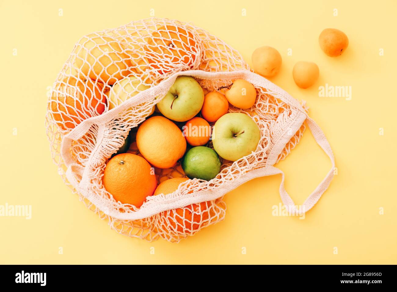 Mesh-Einkaufstasche mit frischen Früchten auf hellgelbem Hintergrund. Zero Waste, plastikfreies Konzept. Stockfoto