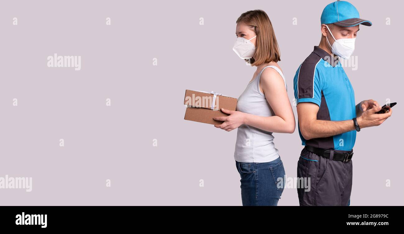 Die nette Frau hat das Paket zur Pandemiezeit bekommen, also steht sie mit dem Kurier zurück an den Rücken und beide in einer medizinischen Maske. Stockfoto