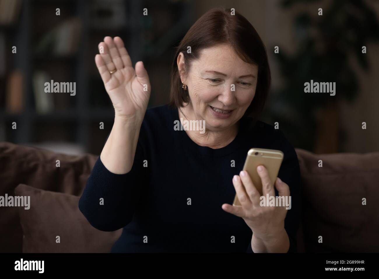 Positive ältere Dame winkt Hallo an Smartphone-Webcam Stockfoto