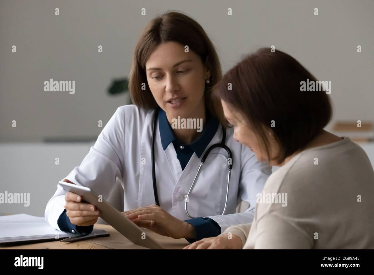 Seriöse freundliche Arzt im Gespräch mit älteren reifen Patienten, mit Gadget Stockfoto