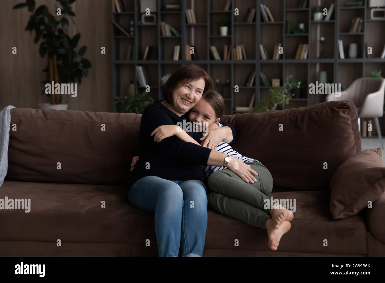 Glückliche Oma umarmt und kuschelt nette Enkelin auf der Couch Stockfoto