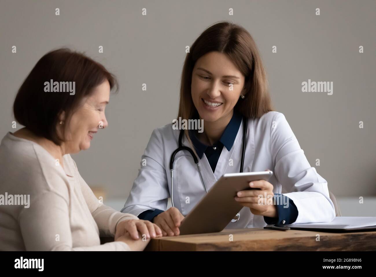 Glücklicher, optimistischer Arzt, der einem alten Patienten im Ruhestand einen Tablet-Bildschirm zeigt Stockfoto