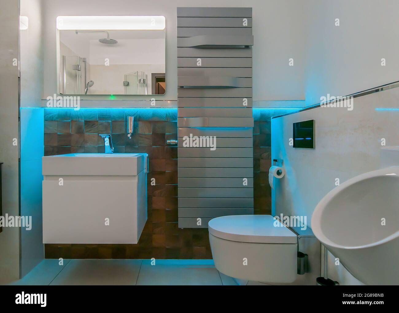 Blick in ein Badezimmer mit farbiger LED-Beleuchtung. Hinter dem Waschbecken befinden sich außergewöhnliche Fliesen mit Holz-Optik Stockfoto