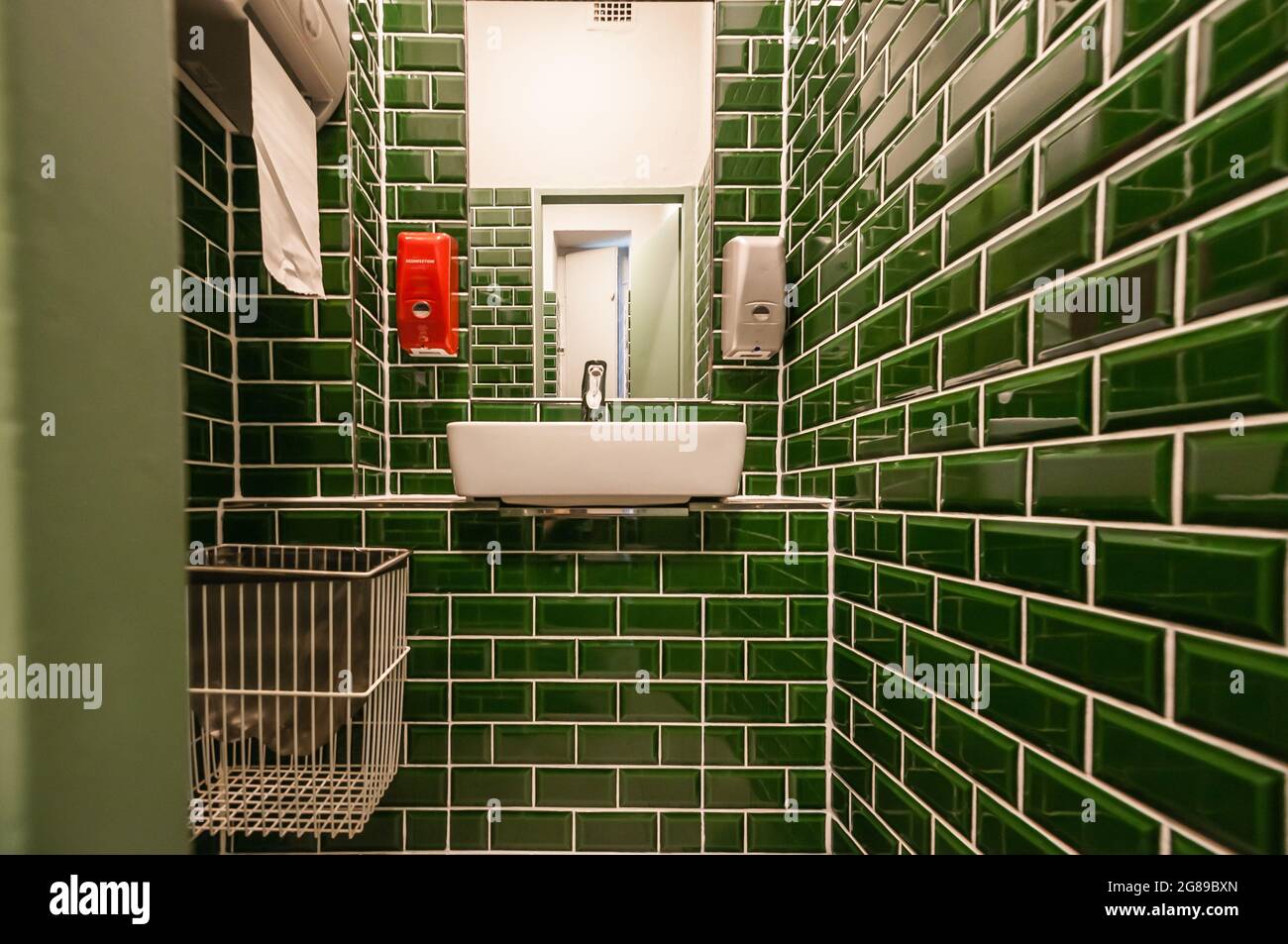 Blick in eine außergewöhnliche Gästetoilette. Mit angeschlossenem Waschbecken. Besonders auffällig sind die kleinen dunkelgrünen Fliesen Stockfoto