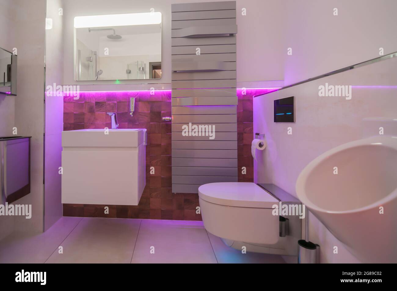 Blick in ein Badezimmer mit farbiger LED-Beleuchtung. Hinter dem Waschbecken befinden sich außergewöhnliche Fliesen mit Holz-Optik Stockfoto