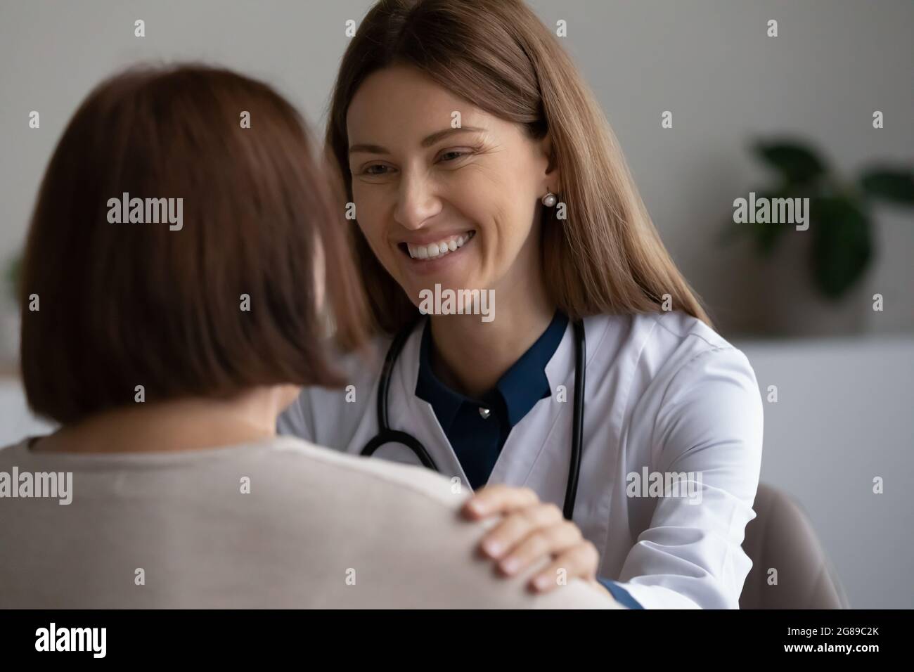 Glücklicher Arzt, der ältere Patienten unterstützt und dabei die Schulter berührt Stockfoto