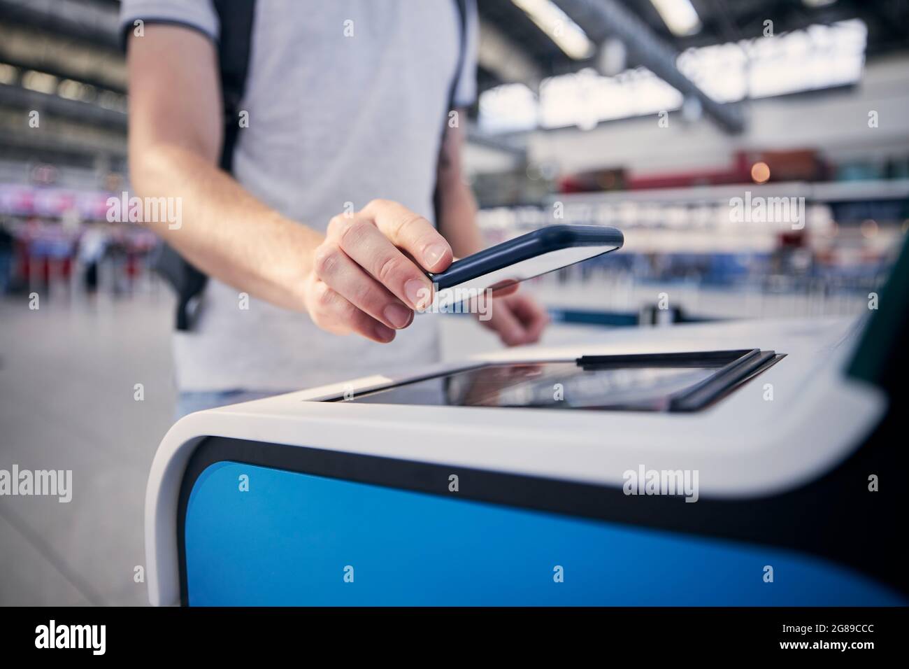 Hand eines Mannes während der Nutzung des Check-in-Automaten. Passagier scannt Ticket auf Smartphone am Flughafenterminal. Stockfoto