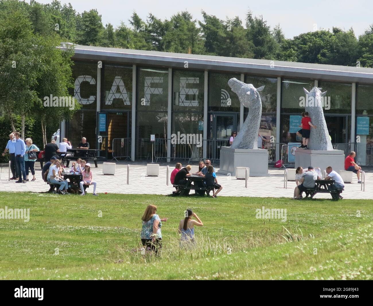 Blick auf das Café, draußen sitzende Besucher und die Modelle der Kelpies im Maßstab 1:10, Helix Park, Falkirk, Juli 2021 Stockfoto