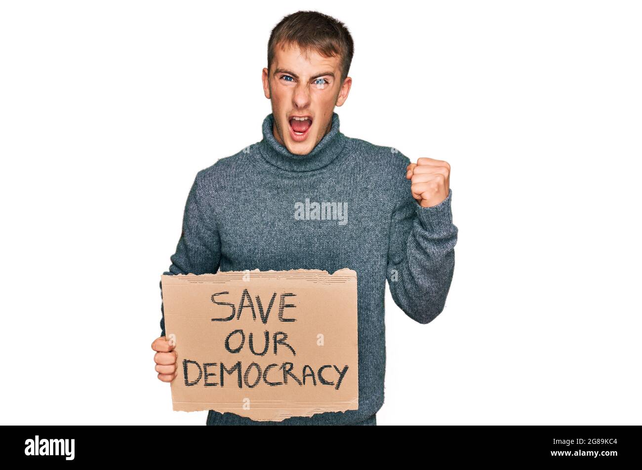 Der junge blonde Mann hält unser Protestbanner für die Demokratie und schreit stolz, feiert den Sieg und den Erfolg mit erhobener Waffe sehr aufgeregt Stockfoto