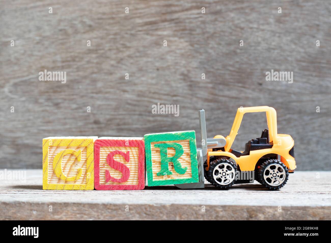 Spielzeug-Gabelstapler halten Buchstabenblock R in Wort CSR (Abkürzung von Corporate Social Responsibility) auf Holz Hintergrund Stockfoto