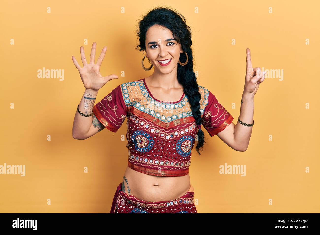 Junge Frau in Bindi- und bollywood-Kleidung zeigt und zeigt mit den sechs Fingern nach oben, während sie selbstbewusst und glücklich lächelt. Stockfoto