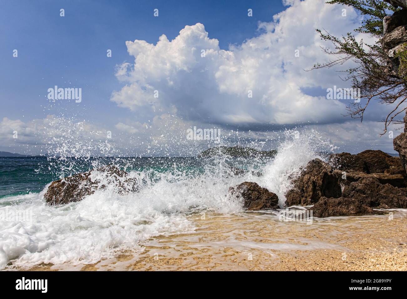 Das Spritzwasser von der starken Welle schlägt den Felsen der Insel an einem sonnigen, hellen Tag. Sauberer und klarer Strand mit blauem Himmel und Wolken im Hintergrund, aufgenommen so Stockfoto