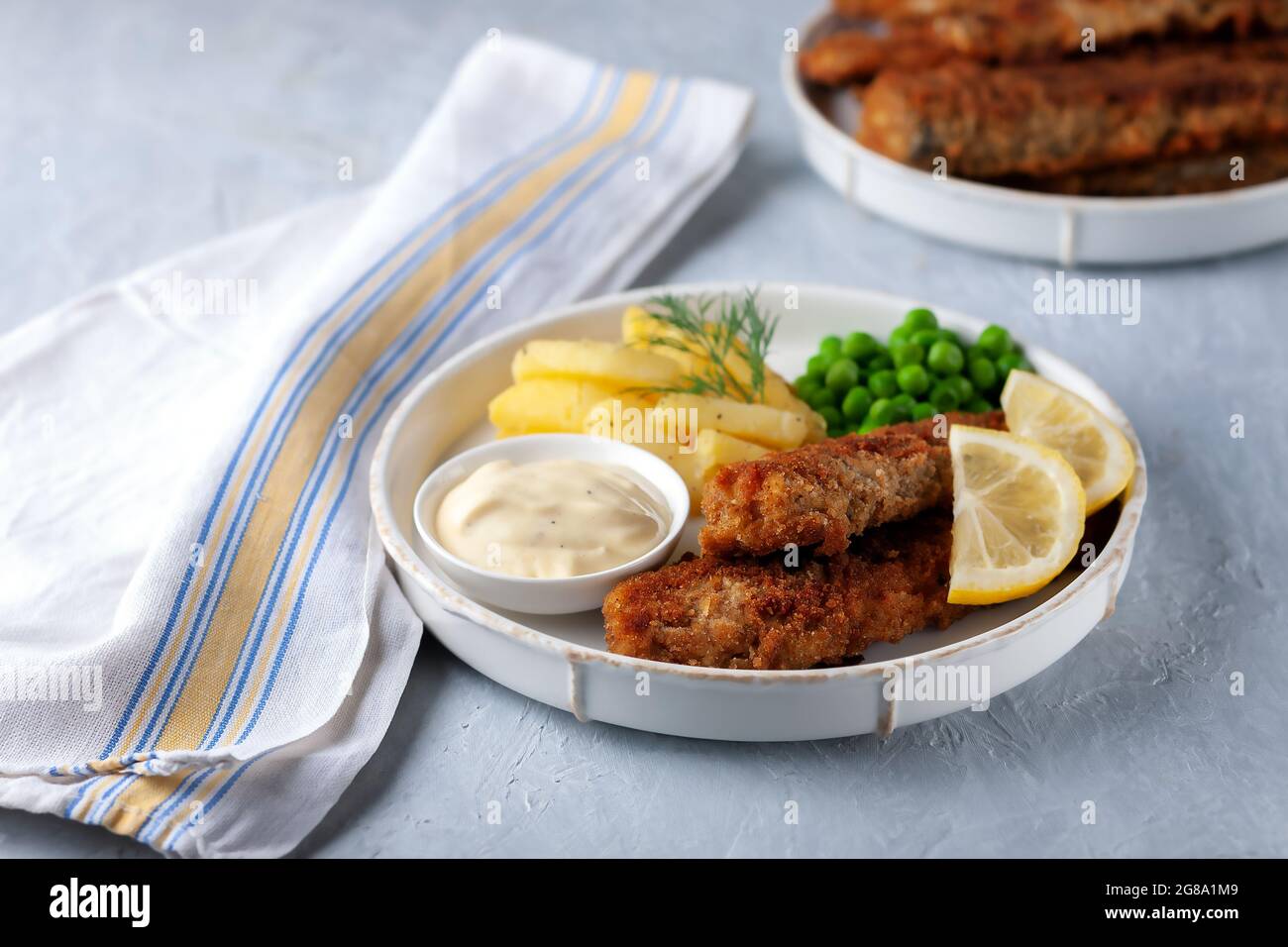 Gebratener Fisch mit grünen Erbsen, Zitrone und gebratenen Kartoffeln Stockfoto