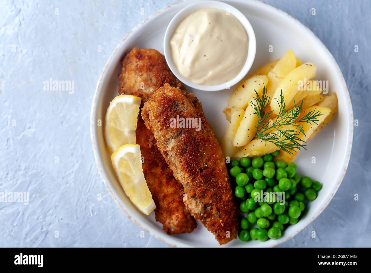 Gebratener Fisch mit grünen Erbsen, Zitrone und gebratenen Kartoffeln Stockfoto