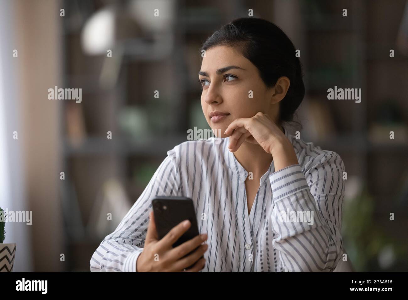 Nachdenkliche indische Frau verwenden Handy denken Planung Stockfoto