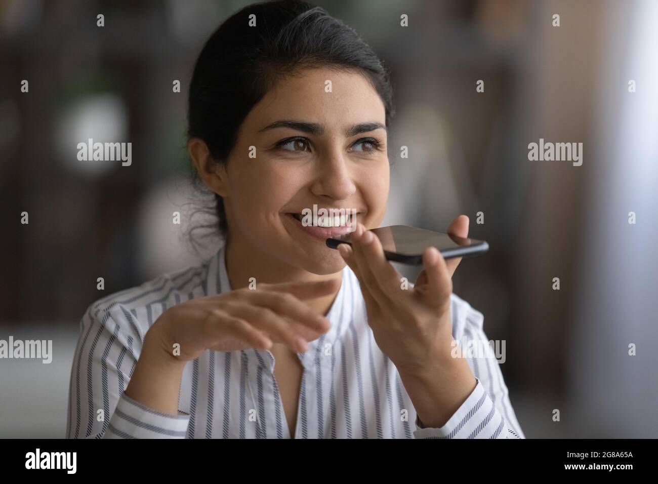 Lächelnde Inderin zeichnet Audionachrichten auf dem Handy auf Stockfoto