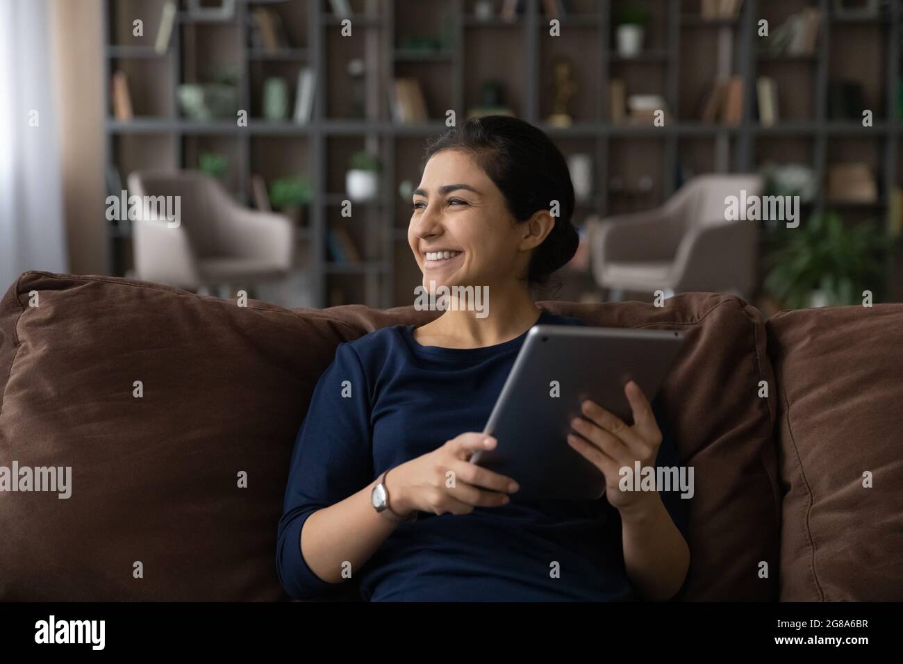 Lächelnde indische Frau verwenden Tablet denken träumen Stockfoto