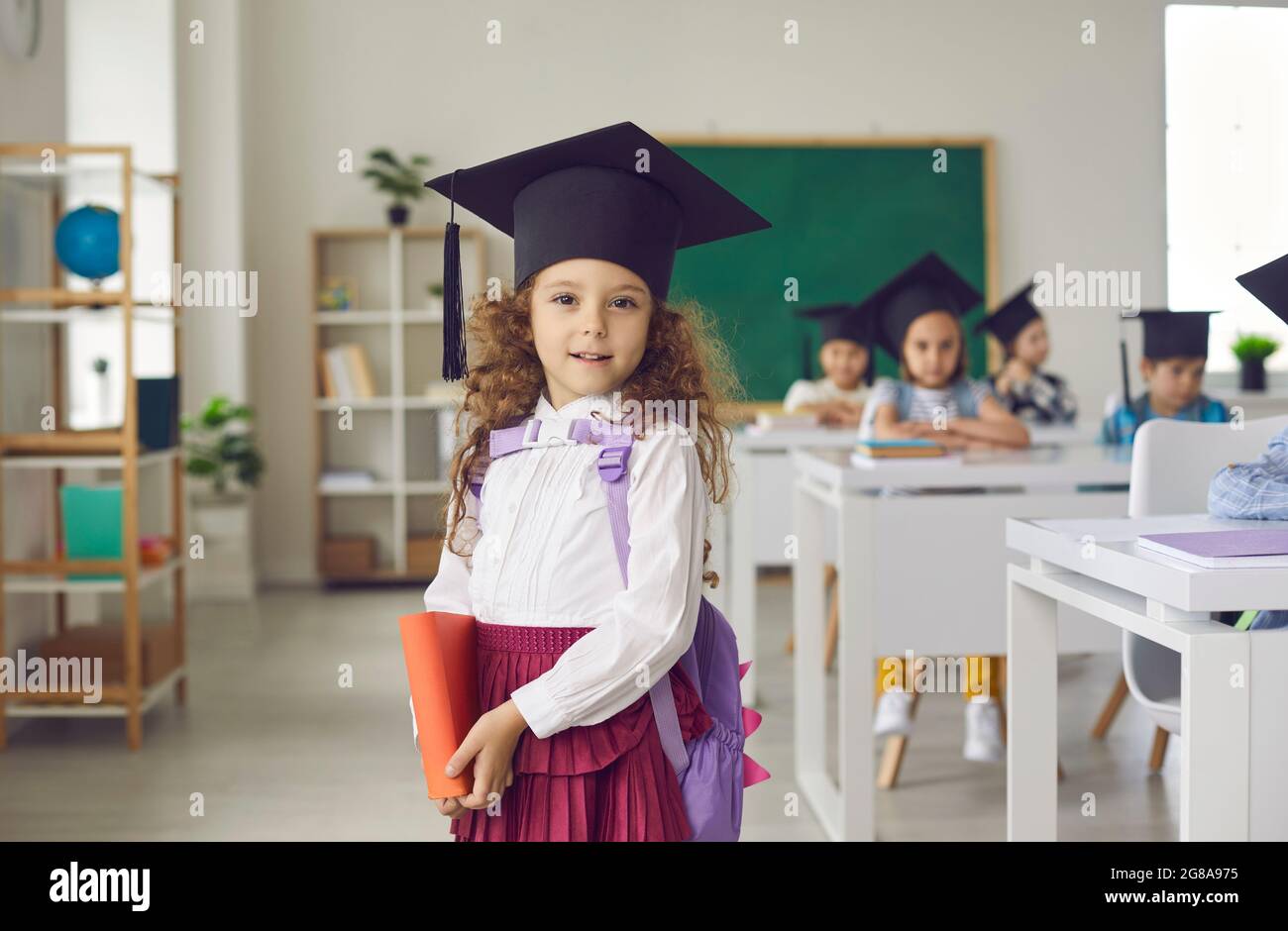 Porträt von glücklich lächelnd Grundschule Mädchen in Abschlusskappe Stockfoto