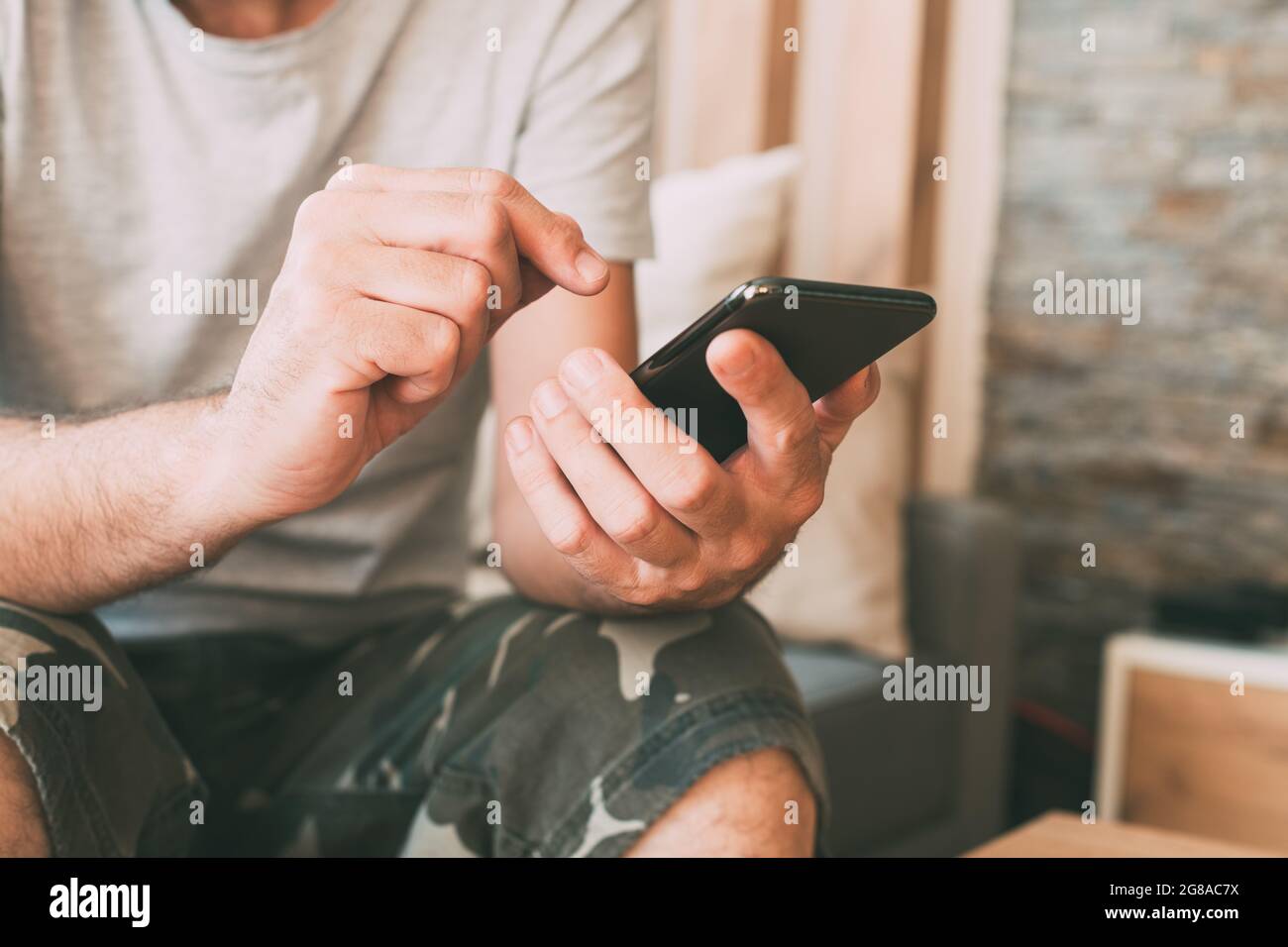 Nahaufnahme von zwanglosen männlichen Händen, die zu Hause in der Privatsphäre seines Wohnzimmers das Handy benutzen, selektiver Fokus Stockfoto