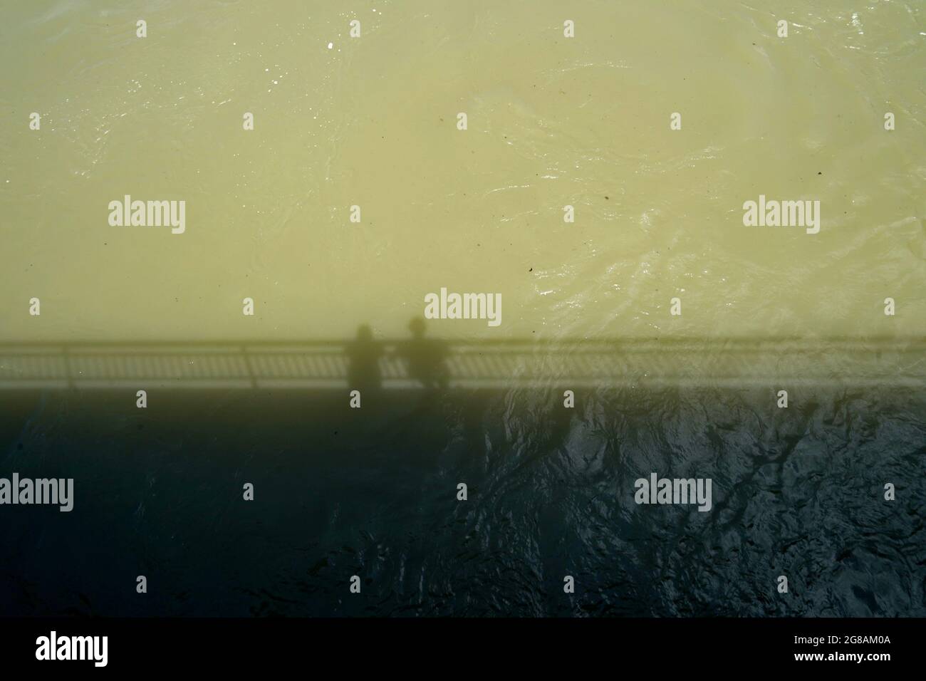 Rheinfluss mit hohem Wasserstand nach starkem Regen. Das Wasser ist schmutzig. Es gibt einen Schatten einer Brücke und zwei Personen, die hinunterschauen und sie beobachten. Stockfoto