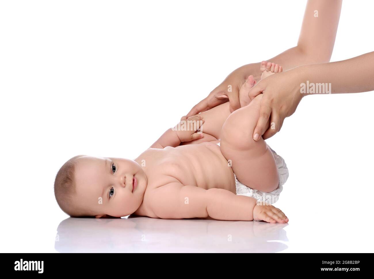 Kleinkind Baby Mädchen Kind in Windel liegt auf ihrem Rücken macht Übungen, Knie beugen und schaut auf die Kamera. Seitenansicht Stockfoto