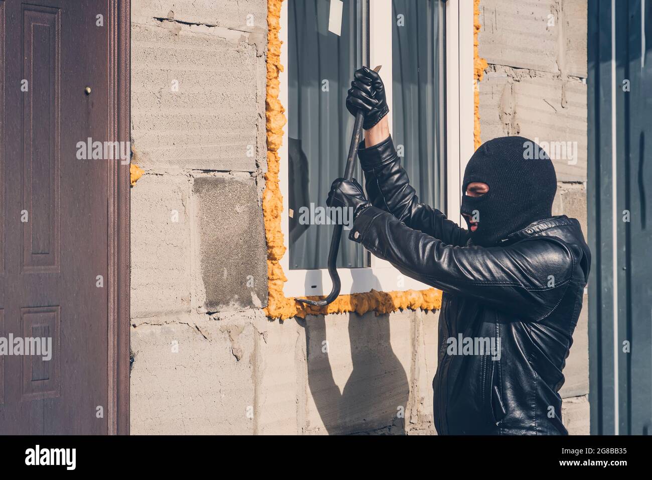 Einbrecher mit verdecktem Gesicht, der versucht, das Fenster zu brechen. Ein maskierter Mann bricht mit einem Brecheisen ein Fenster. Garagenraub. Raub eines Privathauses. Crimin Stockfoto