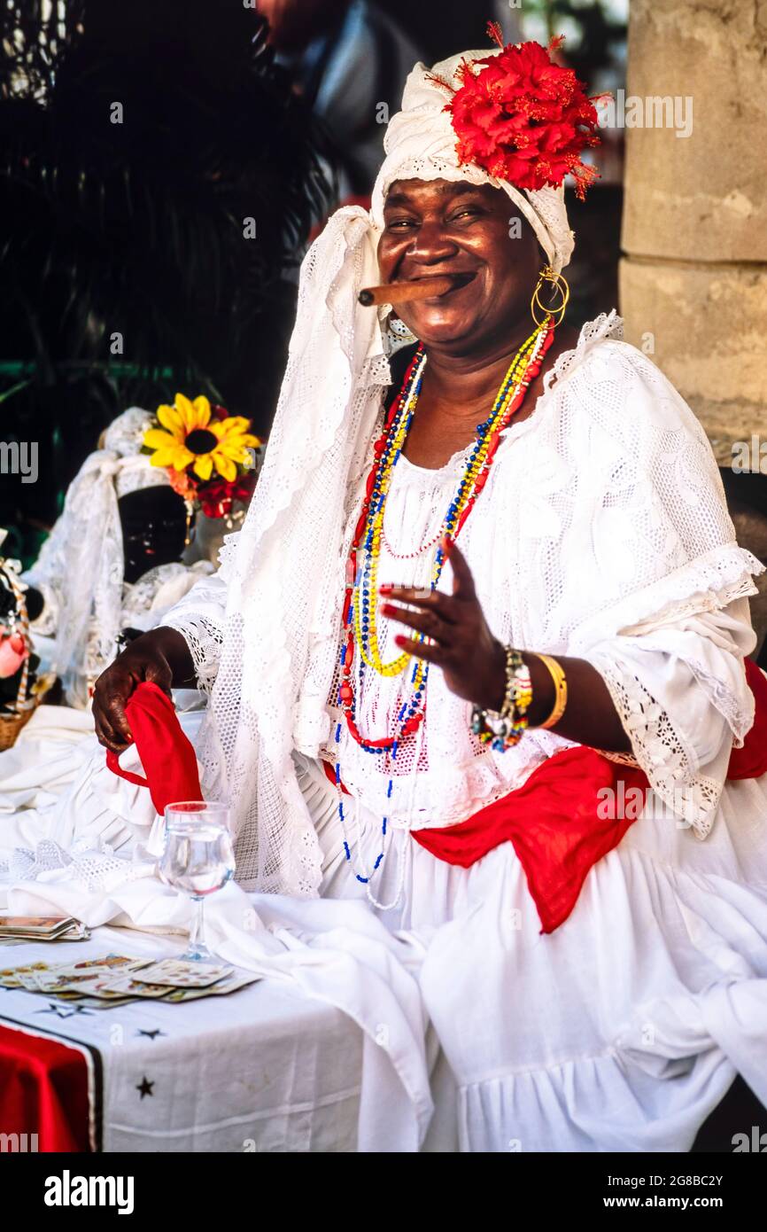 Ethnischer kubanischer Wahrsager, der eine Zigarre raucht und vor dem Tisch mit Spielkarten lächelt, Havanna, Kuba Stockfoto
