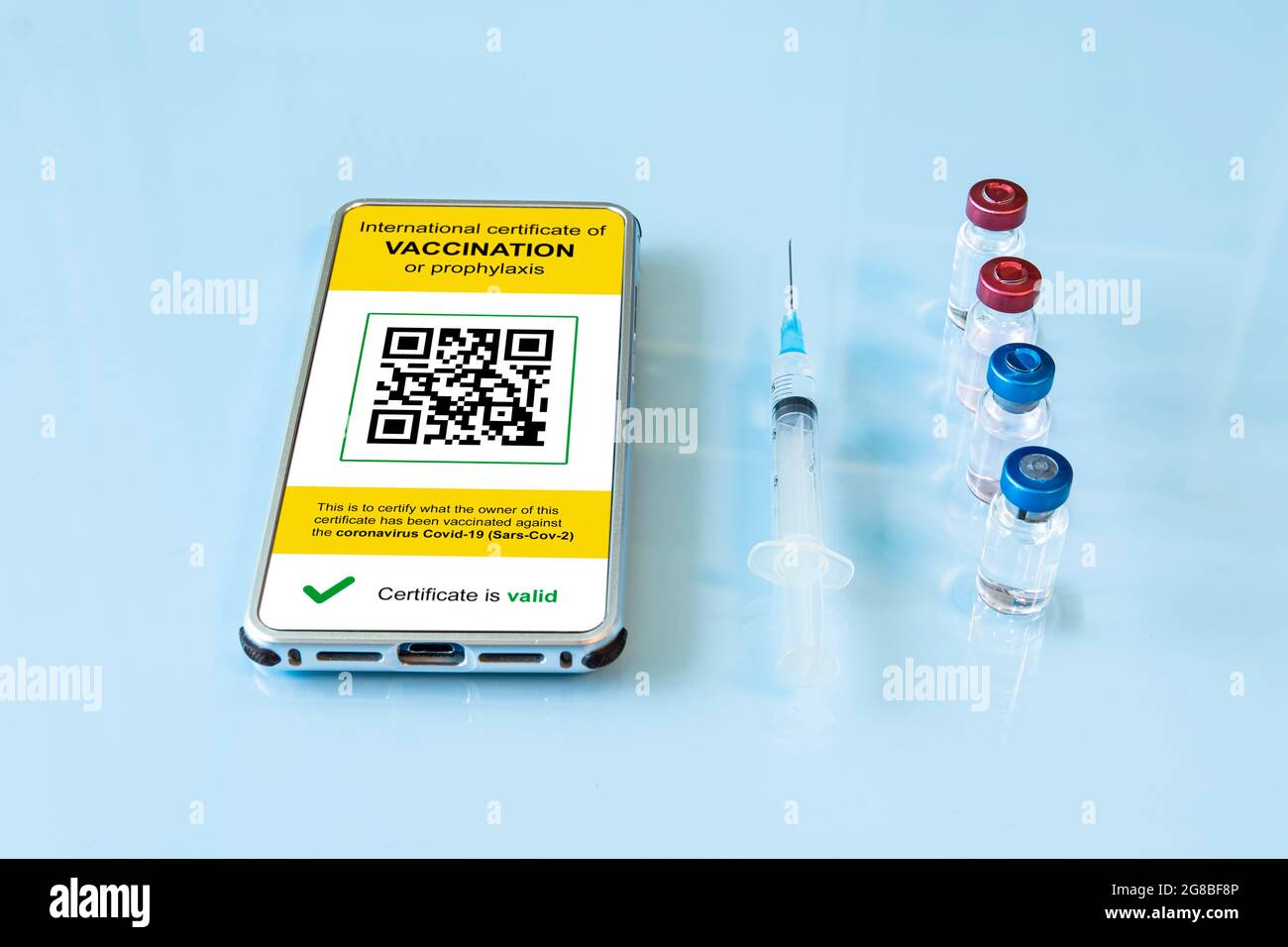 Digitaler Immunitätspass mit einem COVID-19 Impfstempel und qr-Code auf einem Smartphone-Bildschirm mit Impfstoff, Schutzmaske und Spritze auf blauem Bac Stockfoto