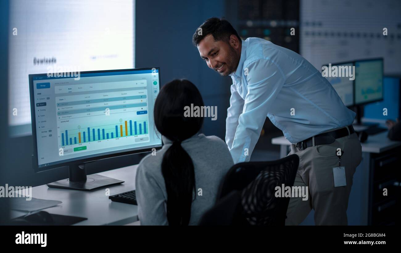 Zwei professionelle Trader, die in einem modernen Überwachungsbüro mit Live Analytics Feed auf einem großen digitalen Bildschirm arbeiten. Überwachungsraum mit Stockfoto