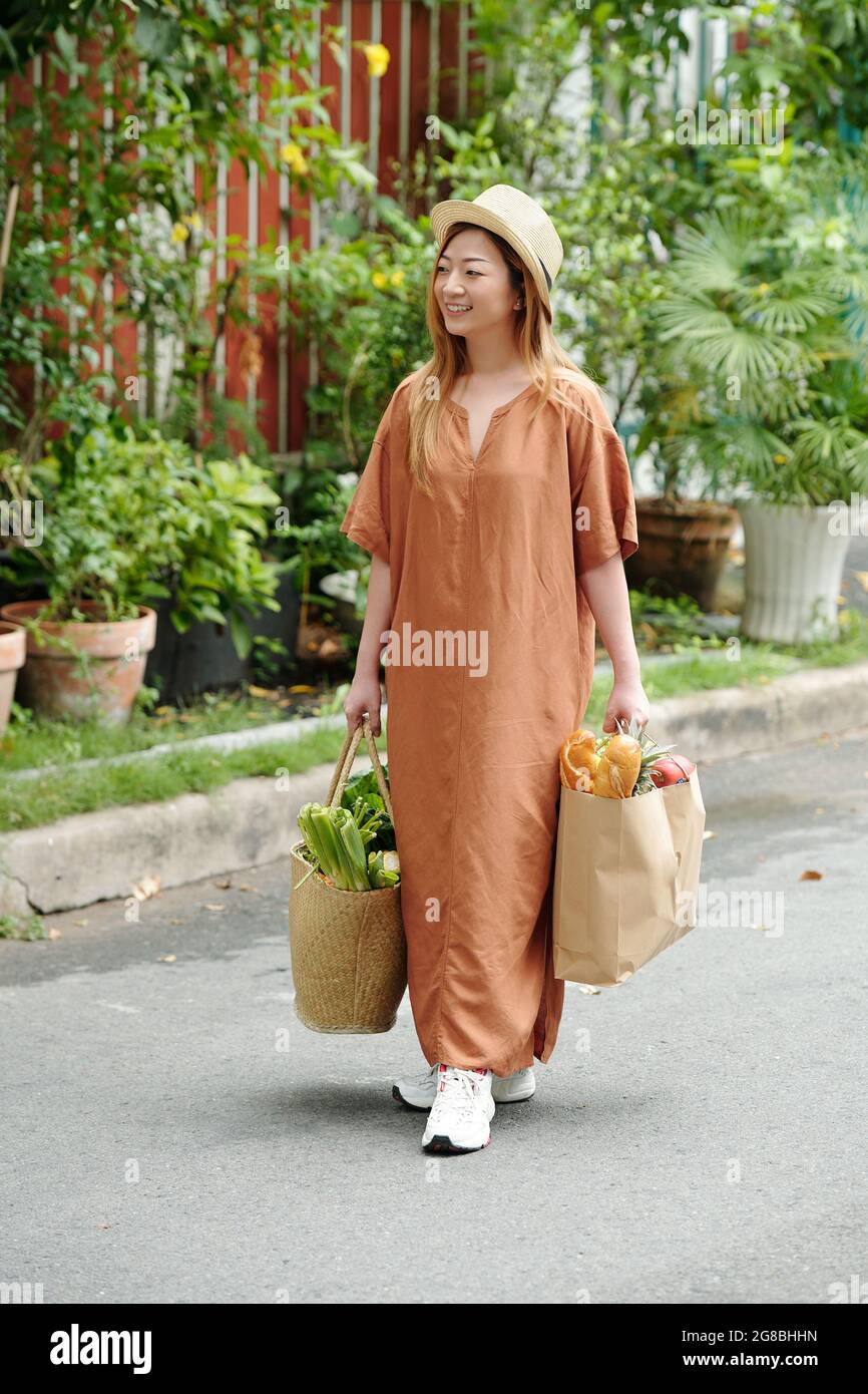 Lächelnde, hübsche junge Frau in Sommerkleid und Strohhut mit Einkaufstaschen Stockfoto