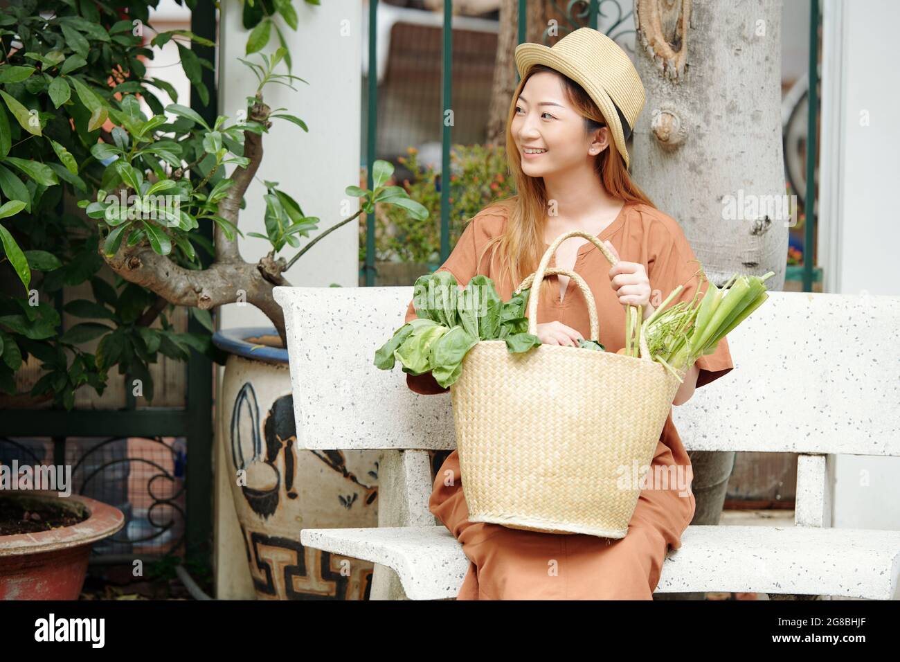 Porträt einer hübschen jungen Frau, die mit einer Tüte frischer Lebensmittel, die sie auf dem lokalen Markt gekauft hat, auf der Bank sitzt Stockfoto