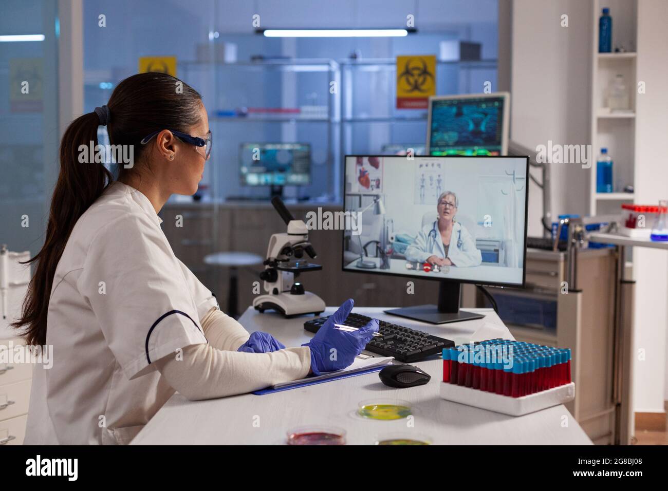 Chemiker, der Videoanruftechnologie auf dem Computer für die Remote-Zusammenarbeit mit dem Spezialisten für Chemieprofessuren verwendet. Forscherin, die sich bei der Untersuchung der Behandlung mit einer Expertin für Viruswissenschaft befasst Stockfoto